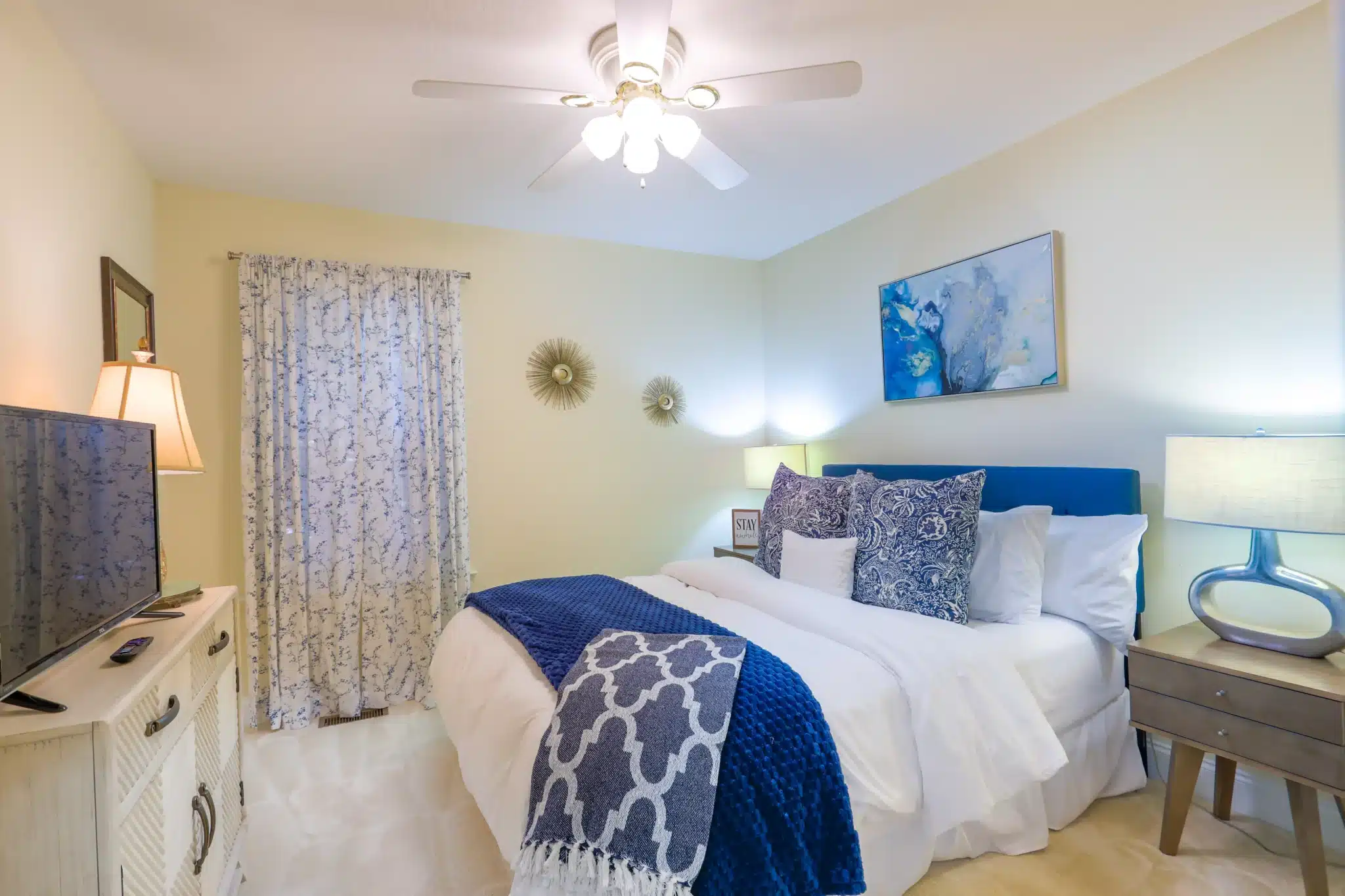 Bedroom with queen bed, blue tufted headboard, navy throw pillows, and cream floral curtains in a Clayton GA chalet rental