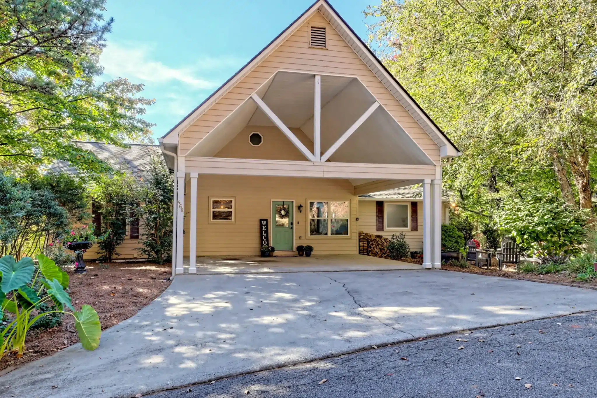 Yellow wood-sided cottage with covered carport, mint green door and wreath, and welcome sign at a Lake scene near cabin