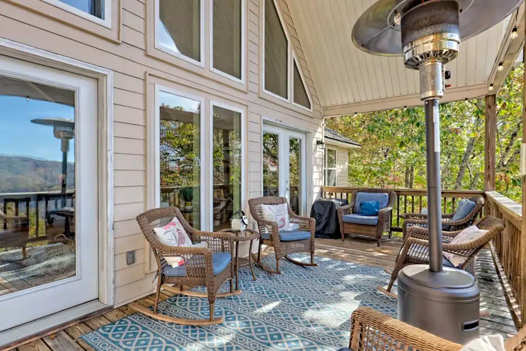 Covered deck with wicker rocking chairs, blue cushions, and a patio heater overlooking autumn mountain views, a Clayton