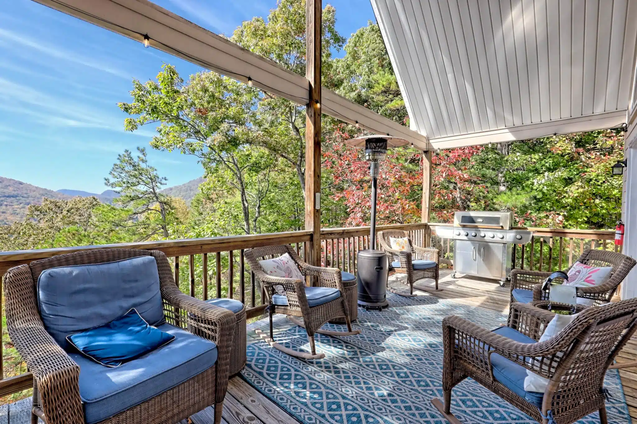 Covered patio with wicker chairs, blue cushions, and a grill overlooking fall foliage in Sunset Ridge, a Clayton GA rental